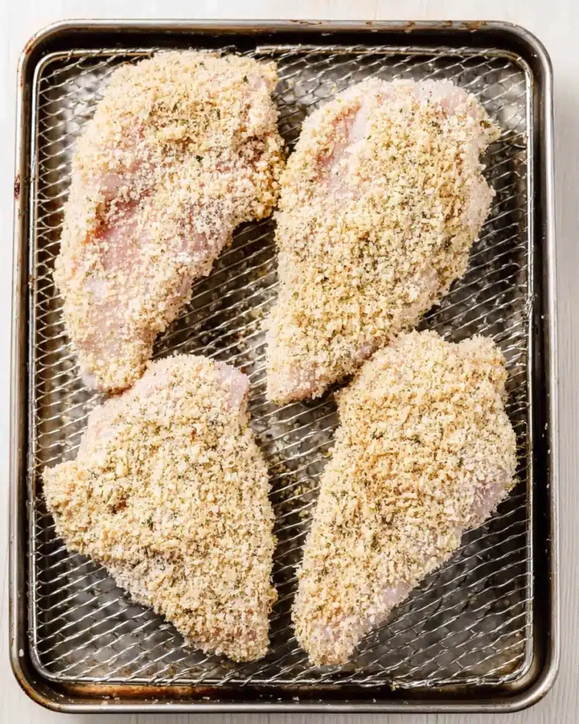 Raw breaded chicken coated with Parmesan and breadcrumbs in an air fryer basket