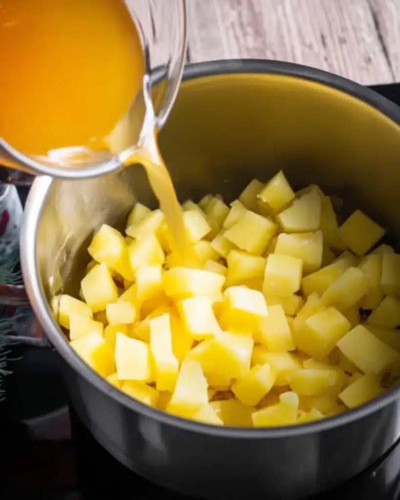 Cheddar Cheese Potato Soup Recipe 3 Pouring chicken broth over diced potatoes in a soup pot