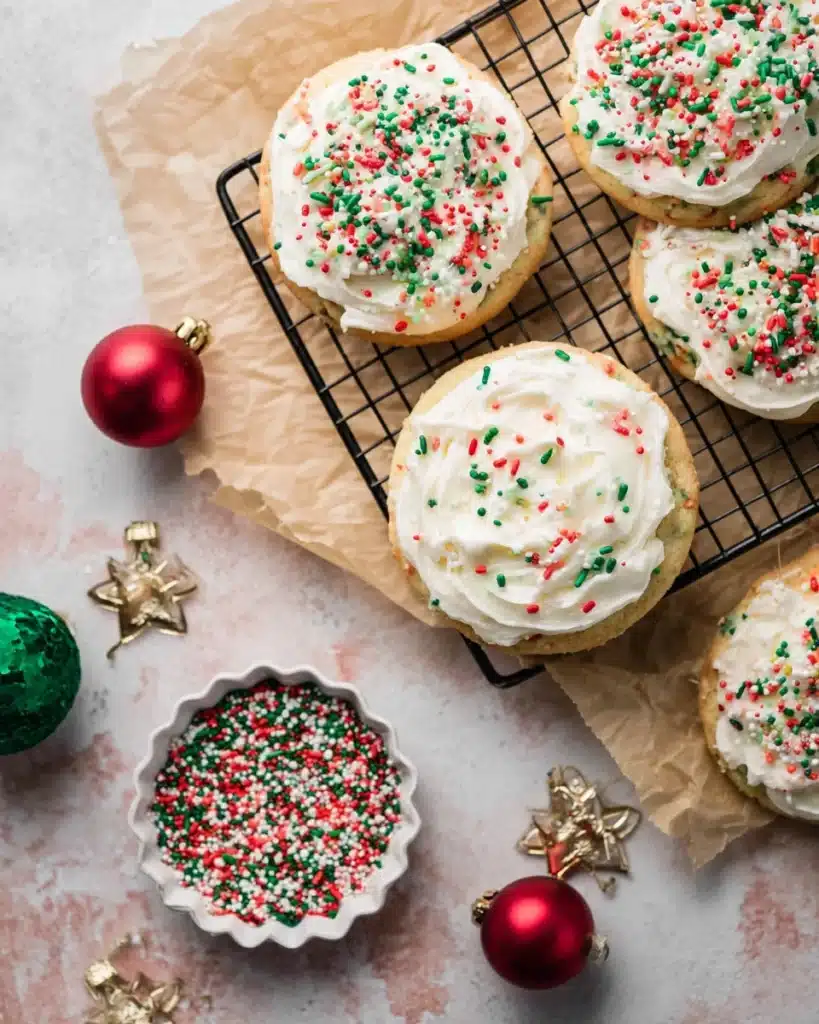 Christmas Sprinkle Cookies 2 Christmas sprinkle cookies with frosting on a wire rack and festive decorations