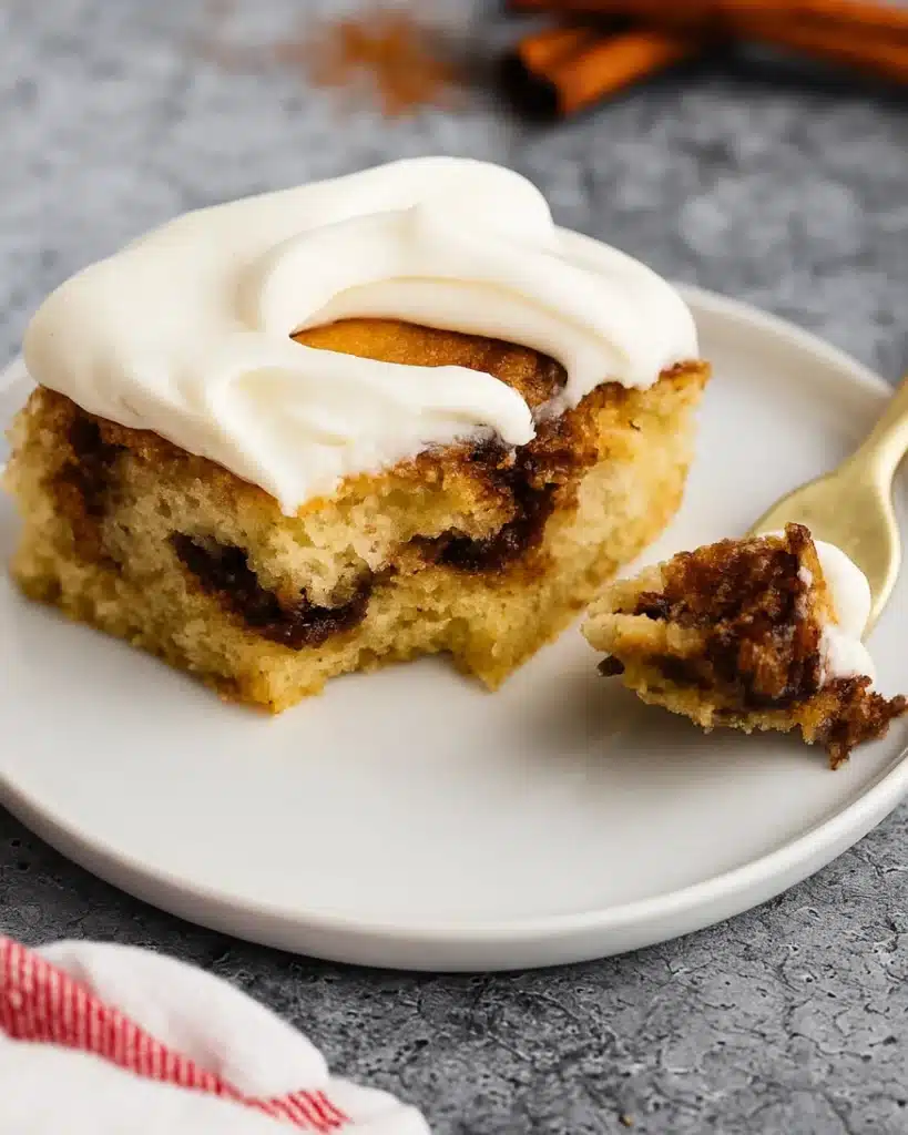 Forkful of Cinnamon Roll Cake with Cream Cheese Frosting on white plate
