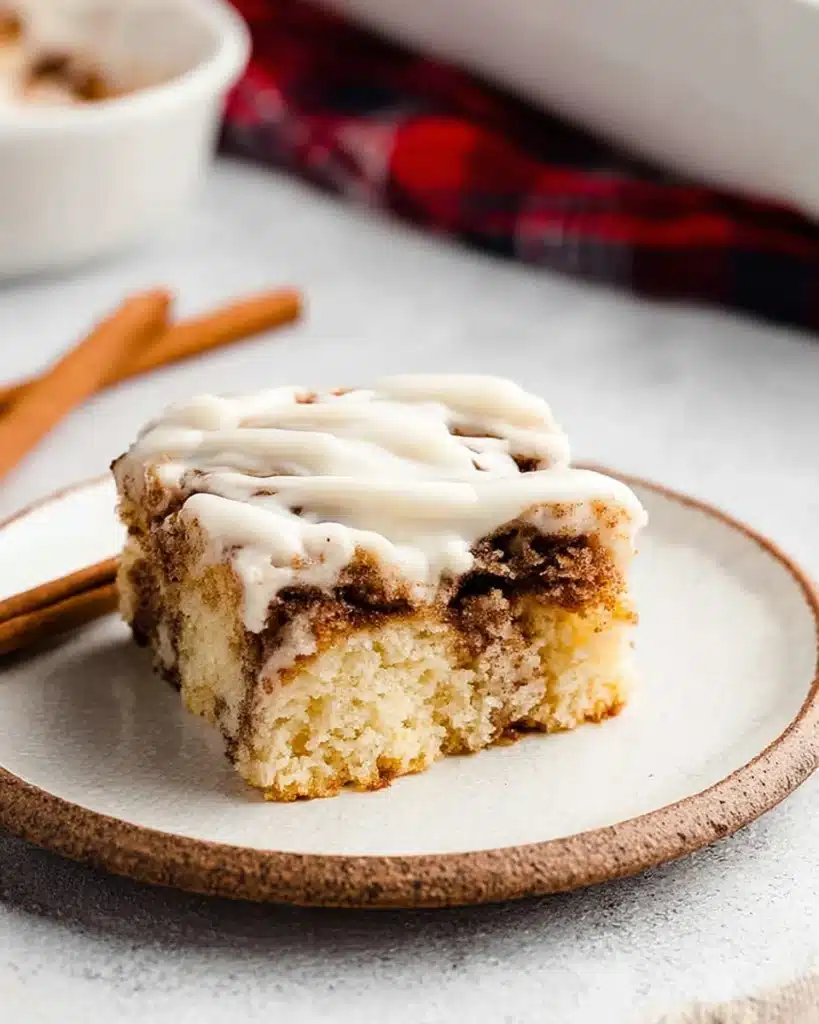 Moist cinnamon roll cake slice with cream cheese frosting on white plate