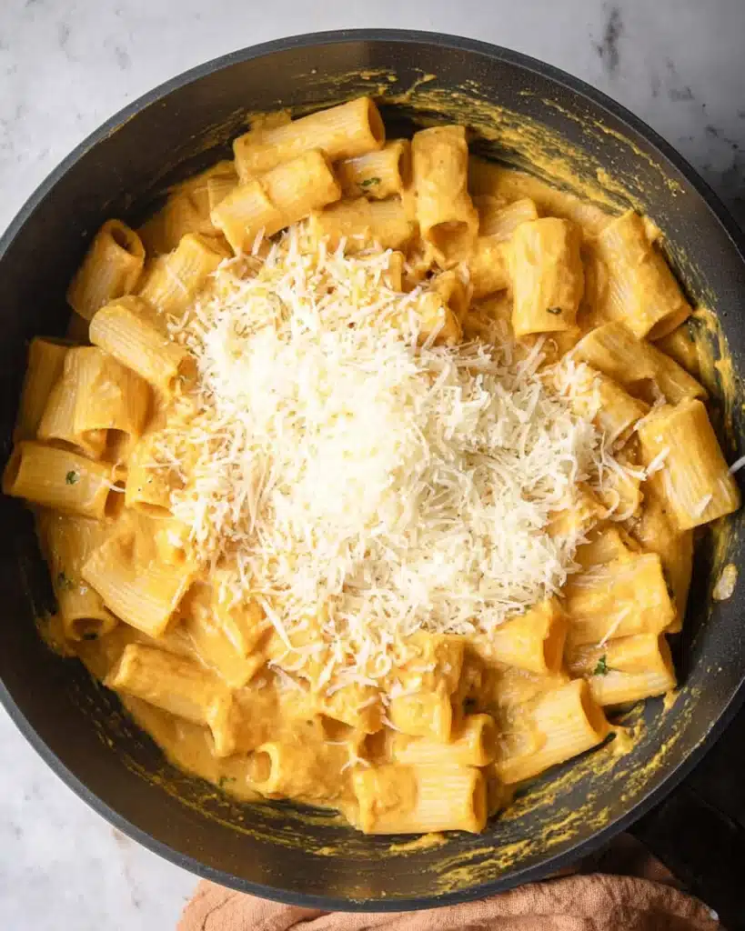 Rigatoni pasta with parmesan added to creamy pumpkin sauce in skillet
