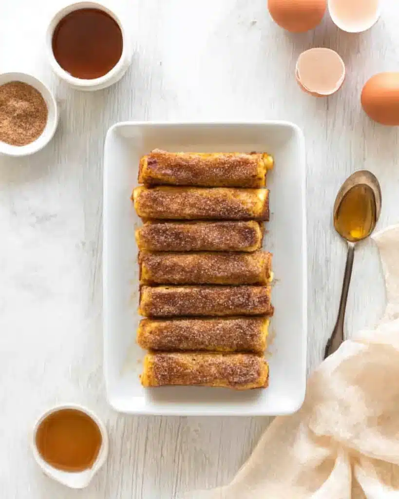 Golden French toast rollups coated with cinnamon sugar on a dish