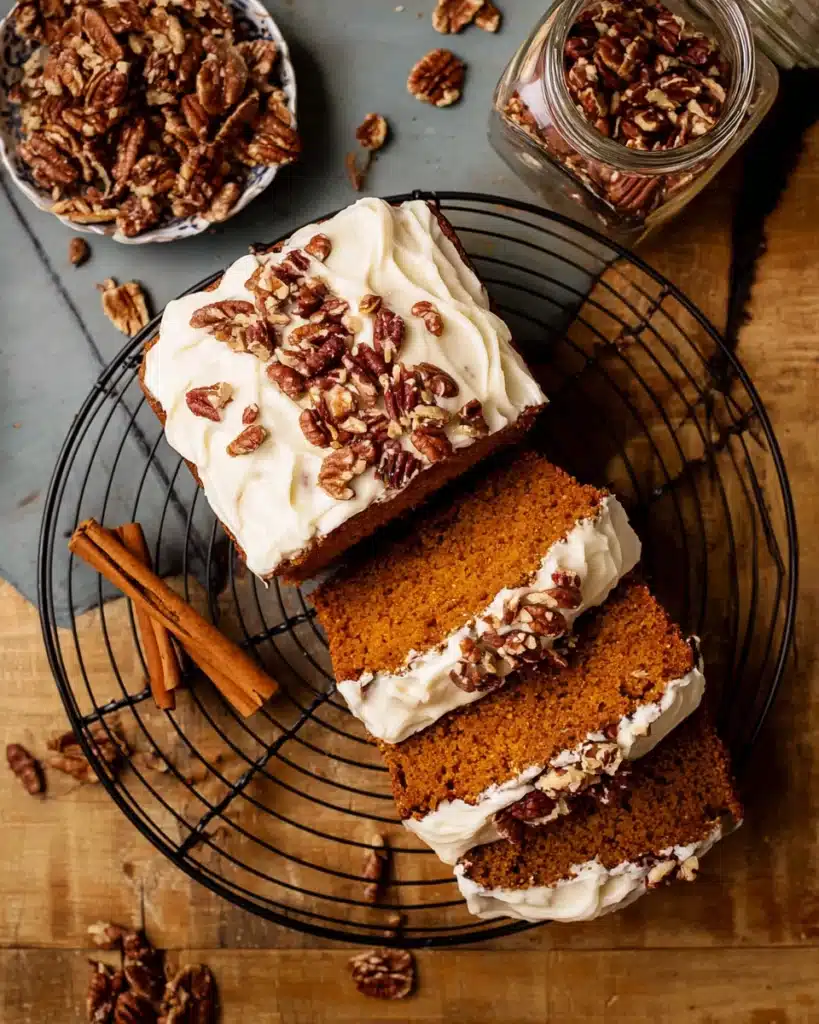 Frosted Pumpkin Bread 1 Sliced frosted pumpkin bread with cream cheese frosting and pecans on a rustic table