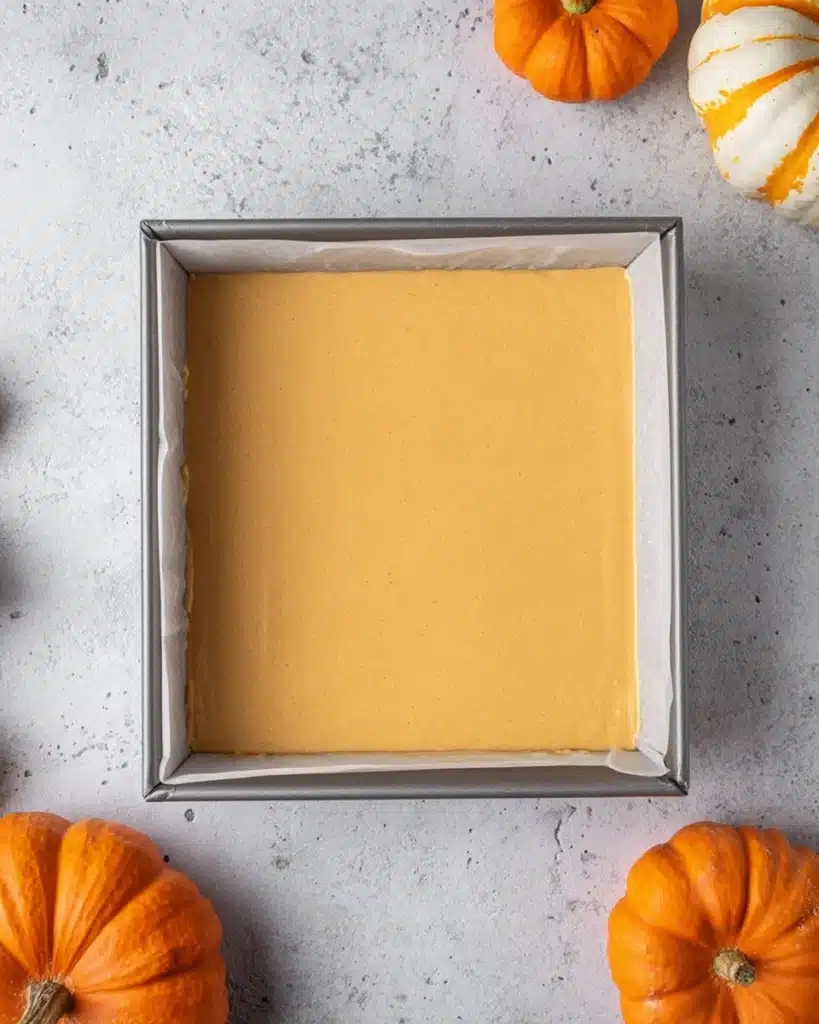 Pumpkin cheesecake batter in baking pan with pumpkins