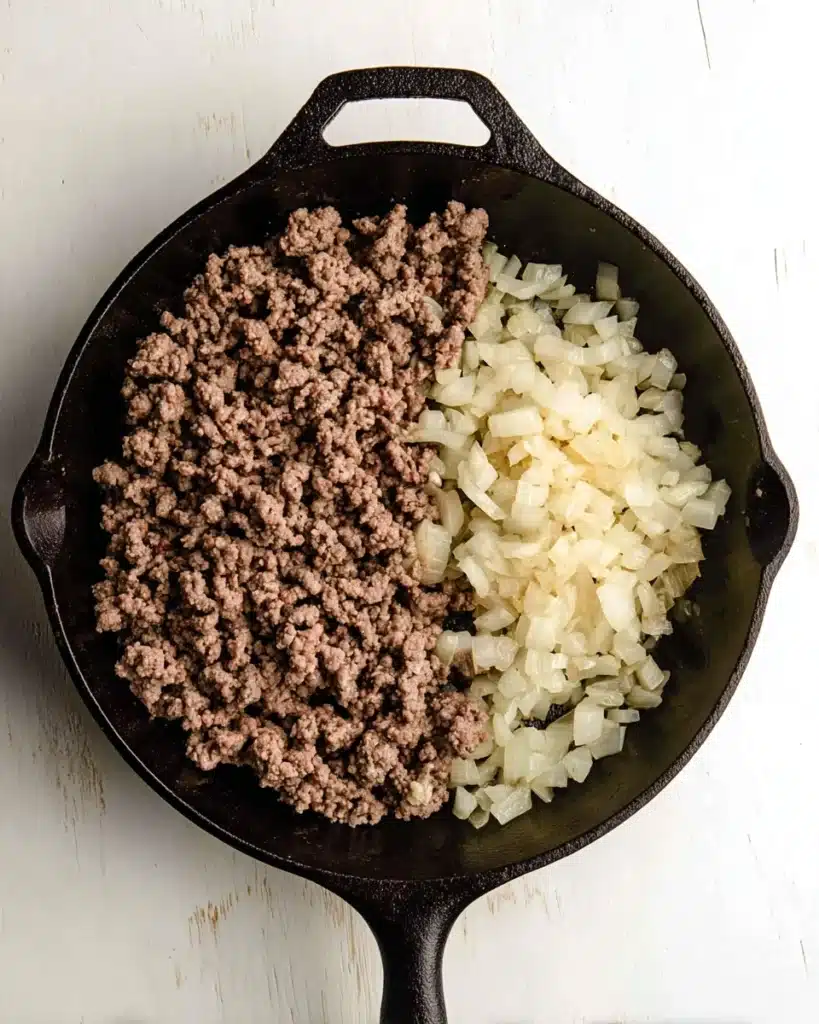 Ground beef and onions cooking in cast iron skillet for Whole30 sloppy joes