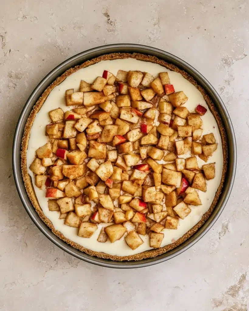 Apple Crumble Cheesecake – The Perfect Thanksgiving Dessert 7 Unbaked apple crumble cheesecake topped with diced spiced apples in pan