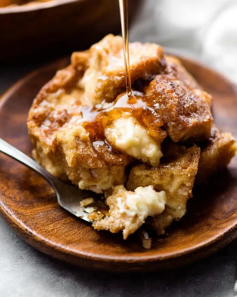 Baked Cream Cheese French Toast Casserole 9 Slice of baked cream cheese French toast casserole with maple syrup on wooden plate