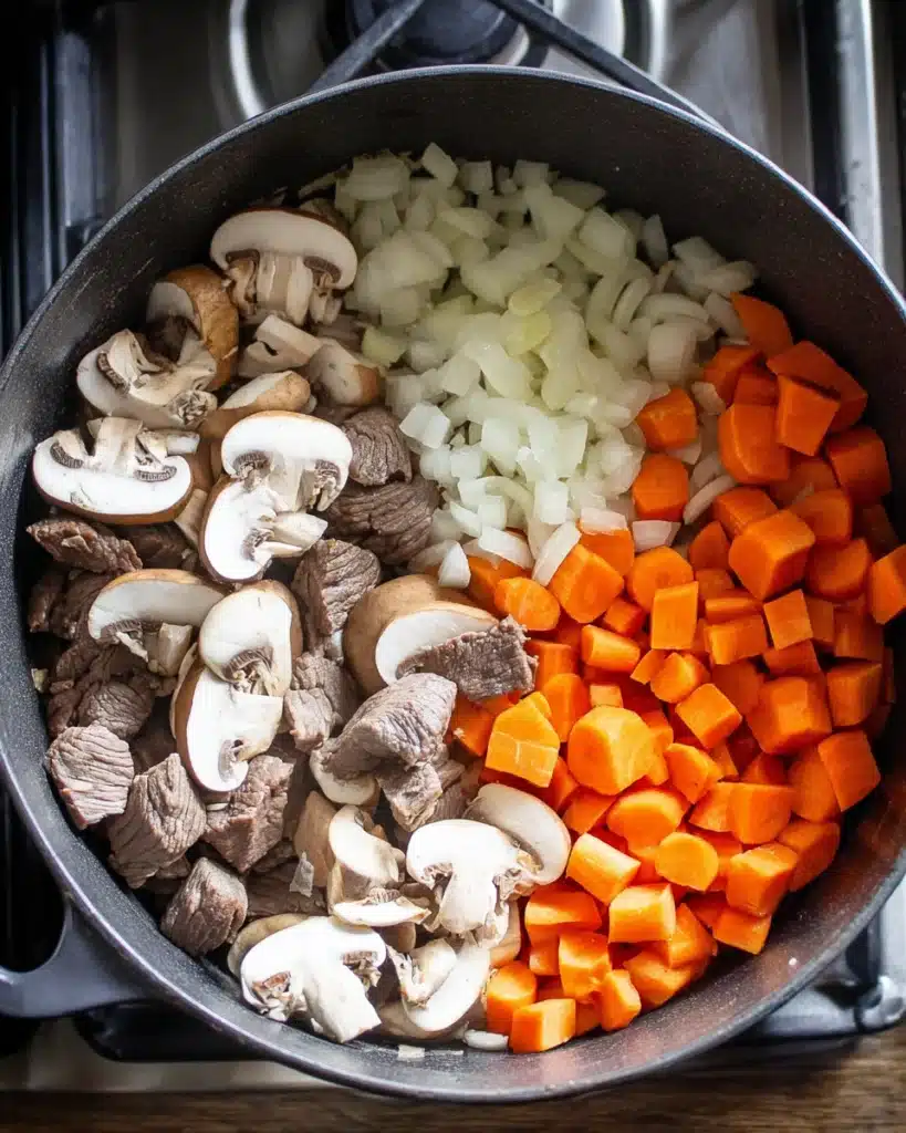 Beef barley soup ingredients with onions, carrots, mushrooms, and beef in pot