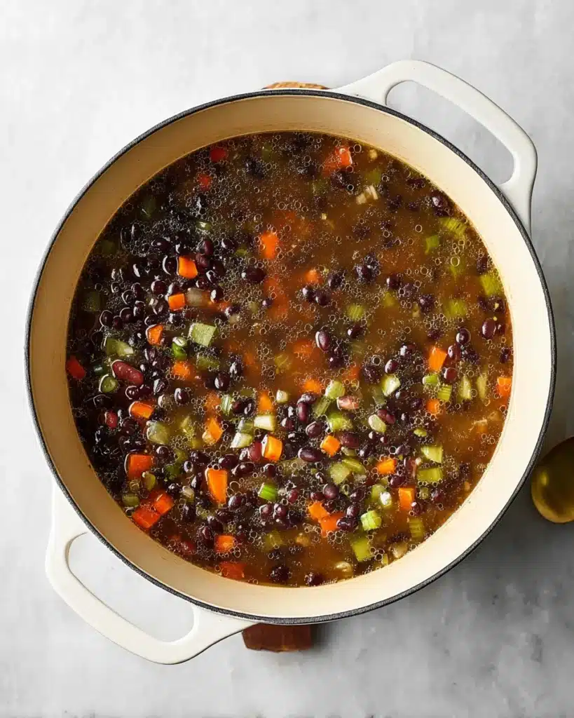 Dutch oven filled with simmering black bean soup with vegetables and broth