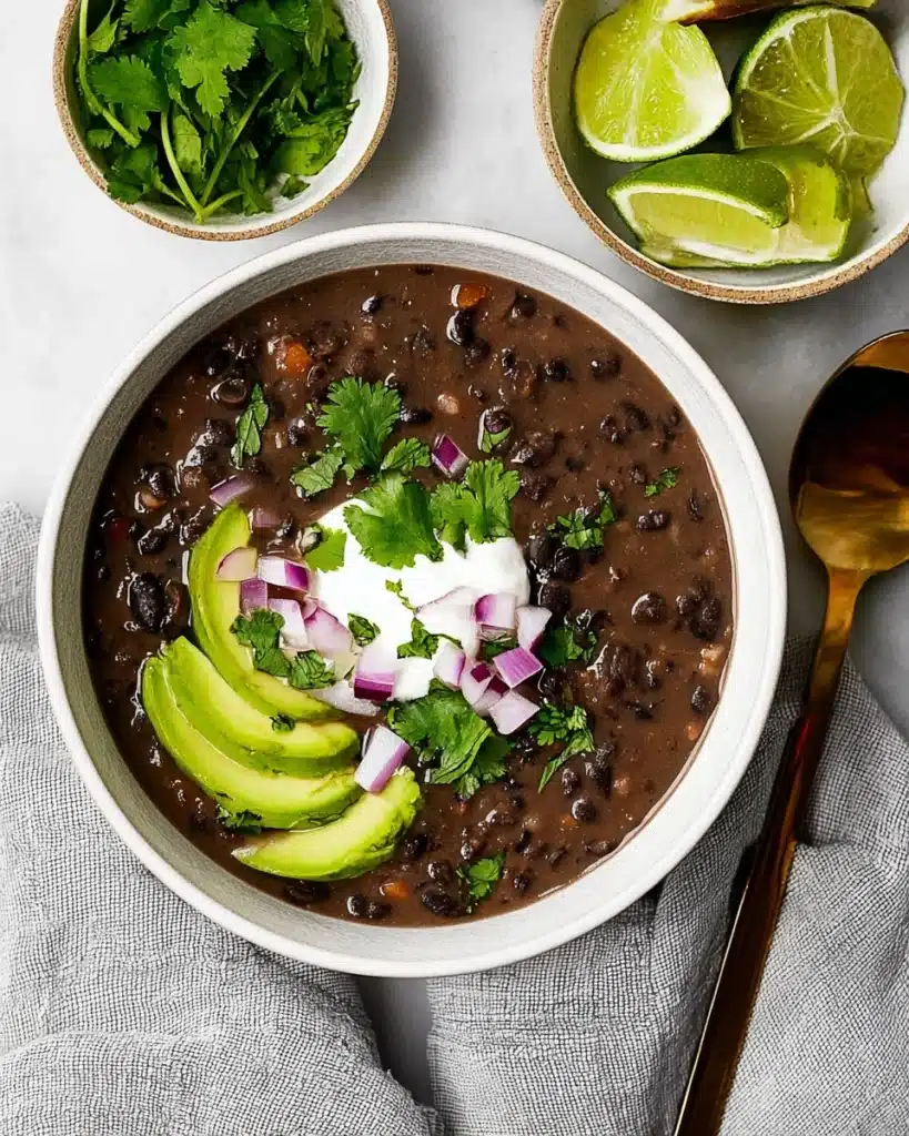 Hearty black bean soup topped with avocado, red onion, cilantro, and sour cream in a ceramic bowl