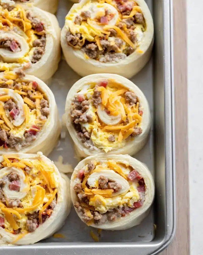 Unbaked breakfast rolls filled with eggs, sausage, and cheese in a pan