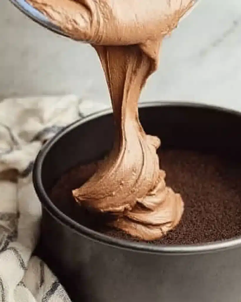 Pouring creamy chocolate cheesecake batter into cookie crust