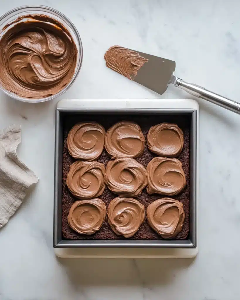 Chocolate mousse being spread over brownie base in baking pan