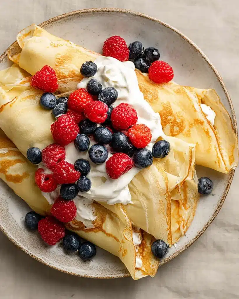Crepes with Pancake Mix (Easy, Light & Delicious Breakfast Recipe) 7 Folded crepes with whipped cream, raspberries, and blueberries on a plate