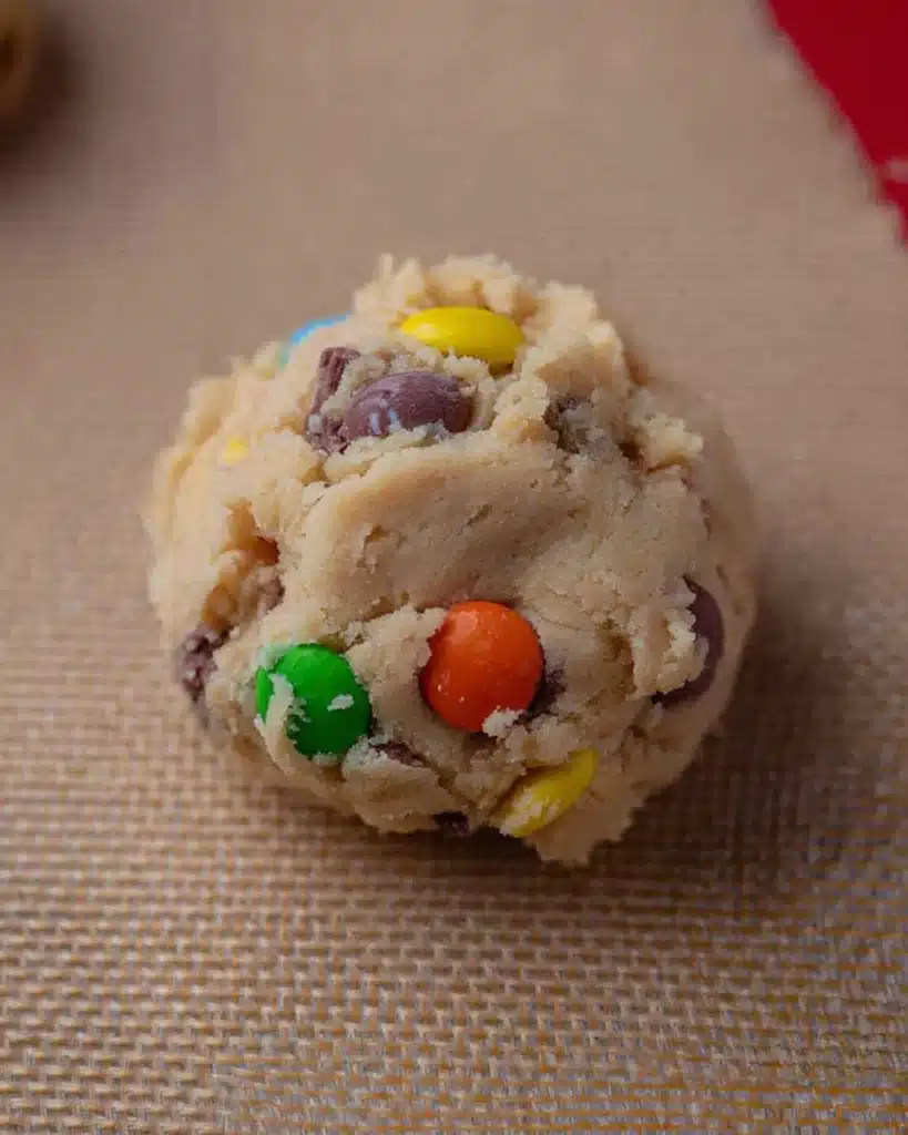 Crumbl Monster Cookie Recipe – Soft & Packed with M&M’s 5 Round scoop of Crumbl Monster cookie dough with colorful M&M’s on baking mat