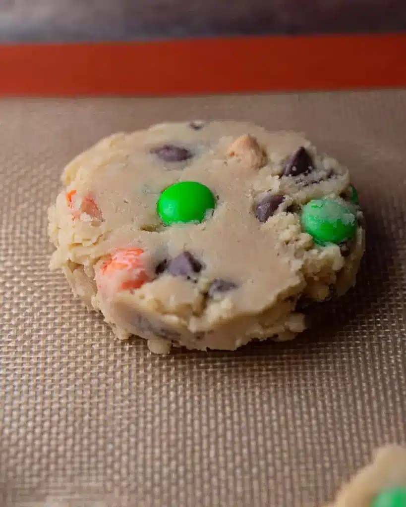 Crumbl Monster Cookie Recipe – Soft & Packed with M&M’s 6 Unbaked Crumbl Monster cookie dough with M&M’s on baking mat