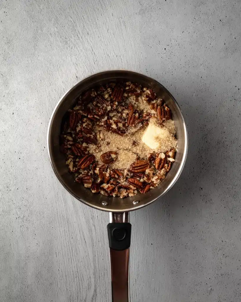 Pecan pie filling ingredients with butter, brown sugar, and chopped pecans in saucepan