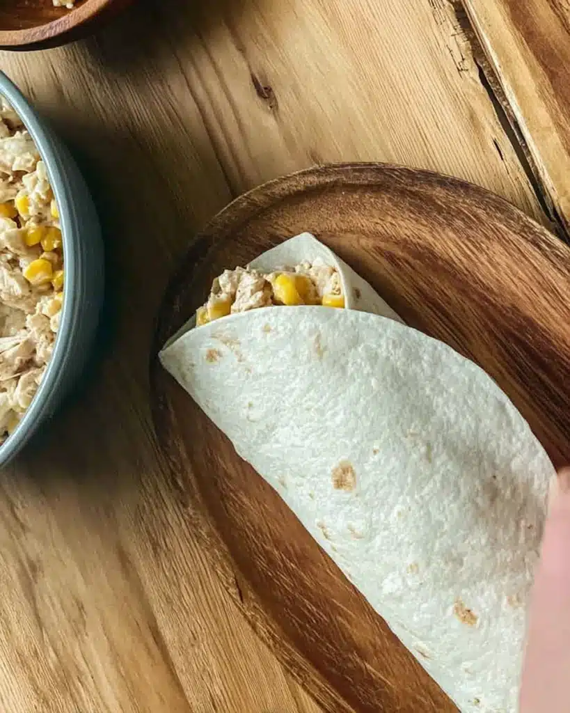 Rolling a chicken wrap with creamy corn filling on wooden board