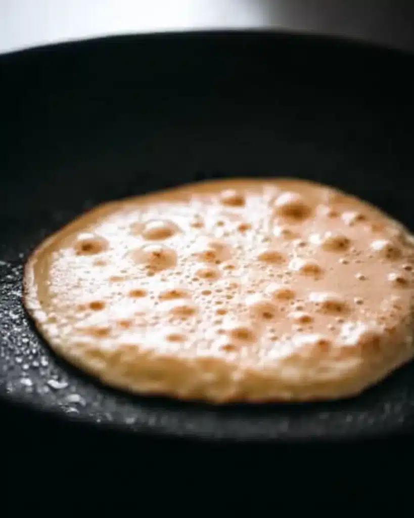 Pancake cooking in skillet with bubbles forming on surface