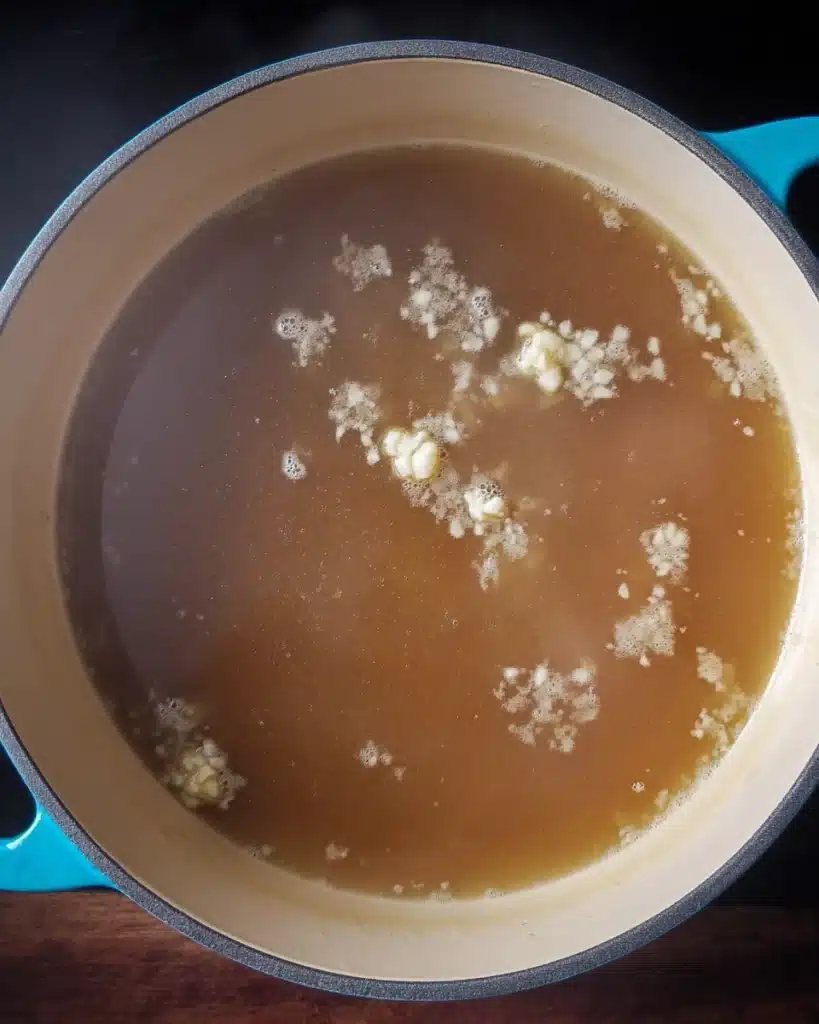 Simmering wonton soup broth with garlic in a teal pot