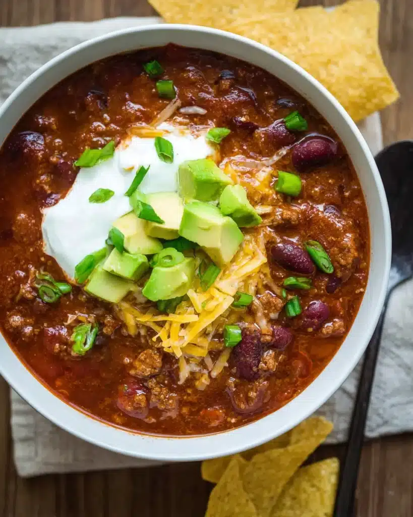 Bowl of slow cooker chili with sour cream, avocado, and cheese