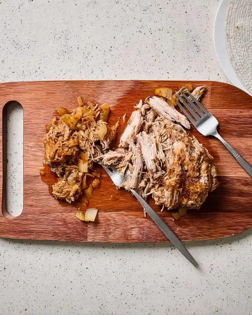 Slow Cooker Texas Pulled Pork 3 Shredded slow cooker Texas pulled pork on wooden cutting board with forks