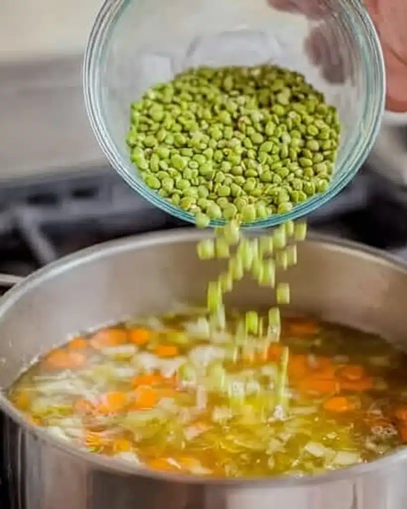 Adding green split peas to simmering soup in a pot