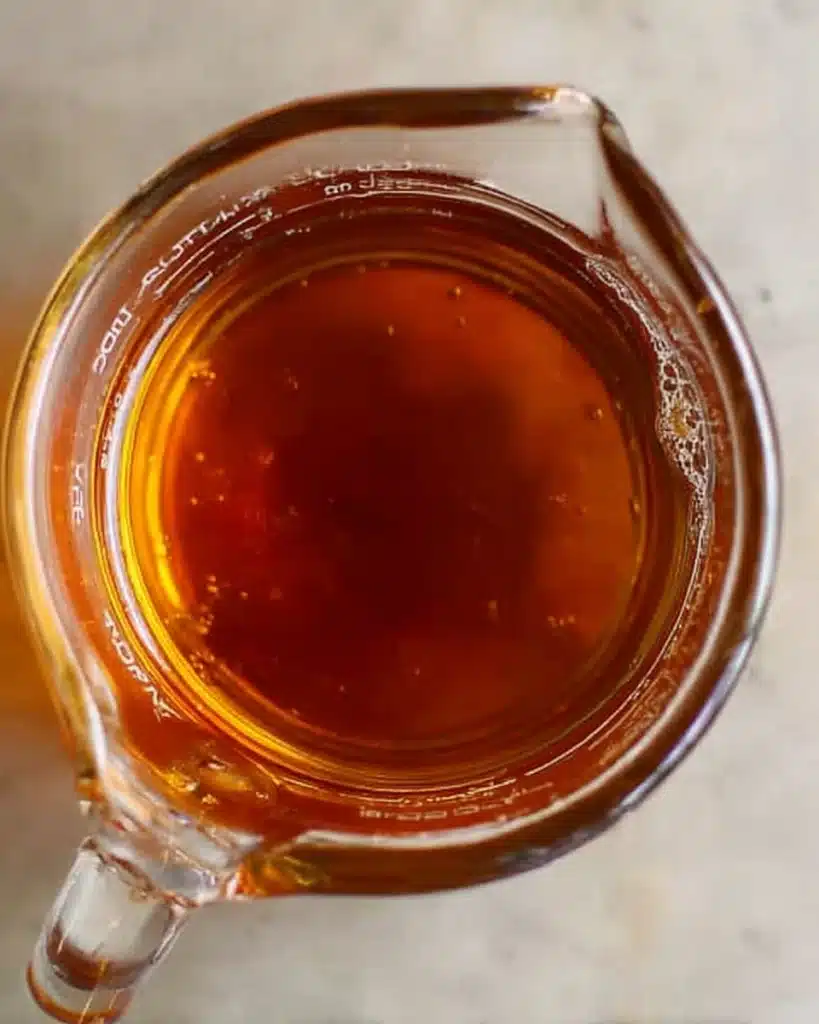 Glass cup of amber almond syrup on a stone countertop