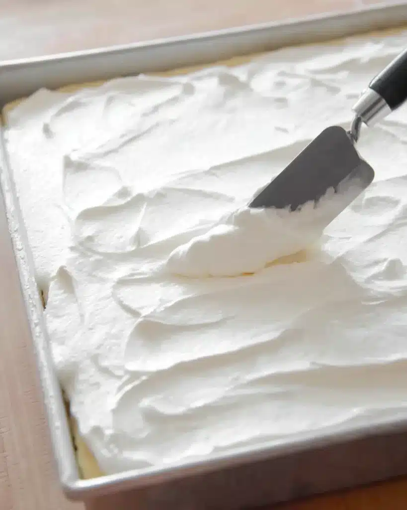 Banana Pudding Poke Cake 4 Spreading whipped topping over banana pudding poke cake