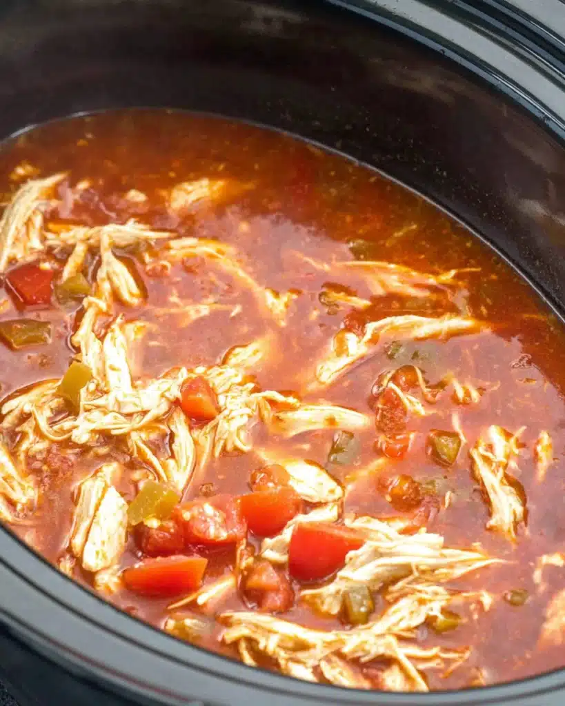 Shredded chicken simmering in enchilada sauce inside a slow cooker