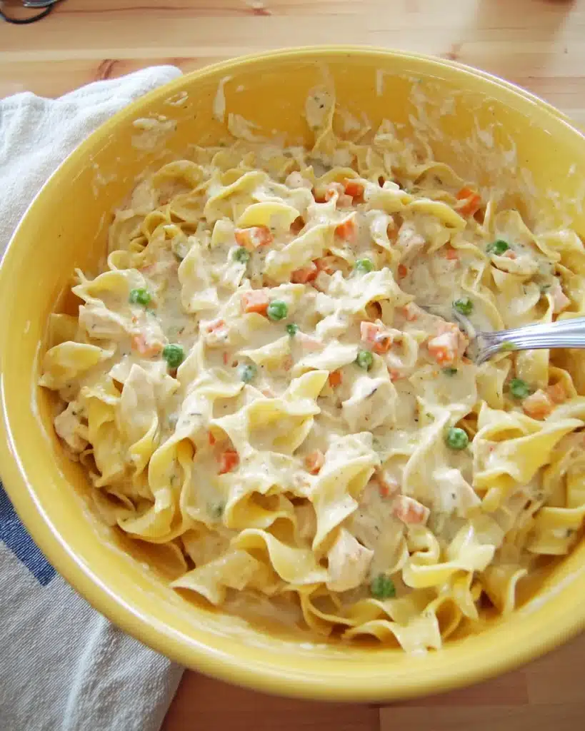 Creamy chicken noodle casserole mixture in a yellow bowl before baking
