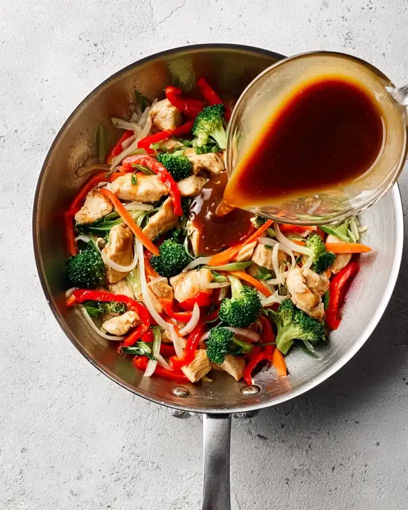 Pouring stir fry sauce over chicken and vegetables in a skillet