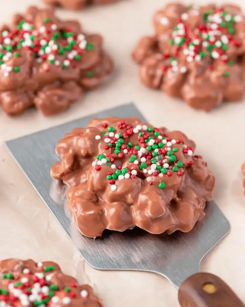 Christmas Crock Pot Candy clusters topped with red and green sprinkles on parchment paper