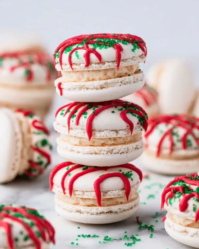 Stacked Christmas Tree Cake Macarons with red icing and green sprinkles on marble surface