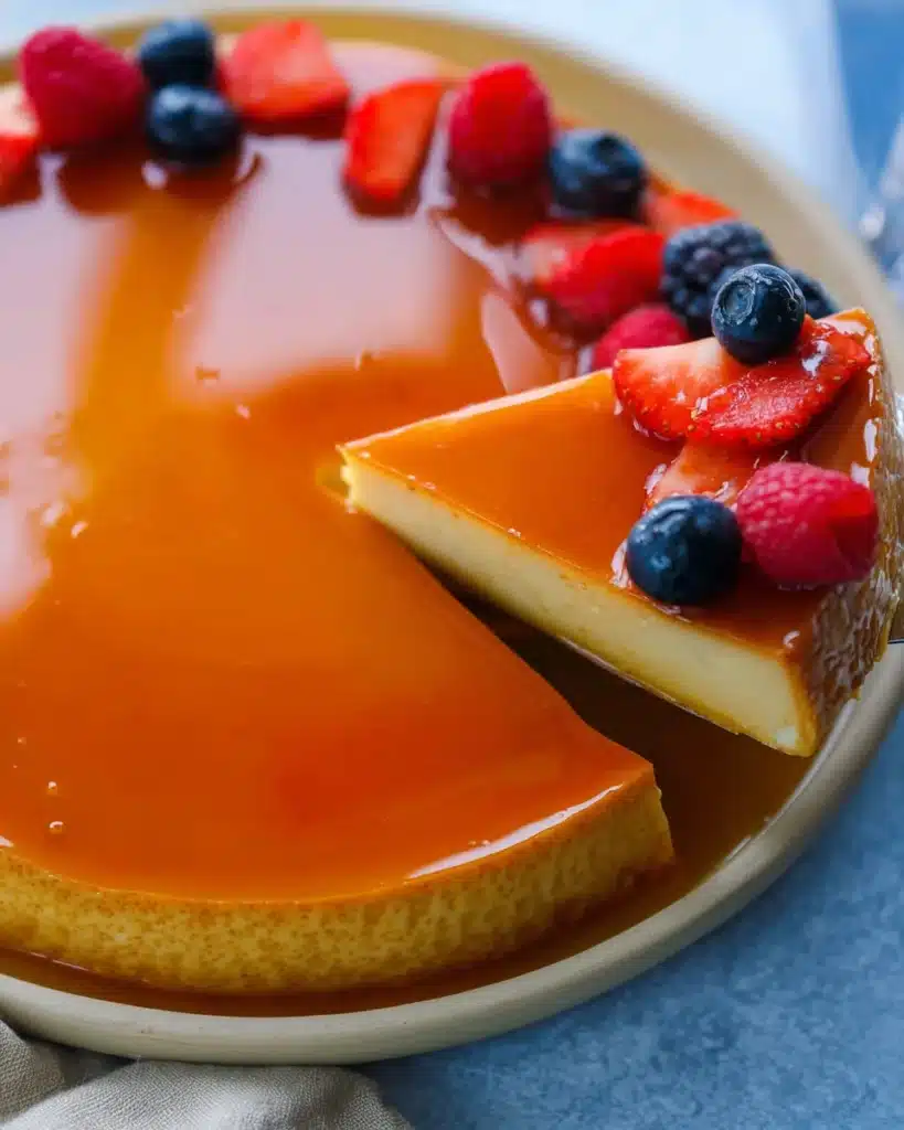 Flan Recipe (Perfect Creamy Caramel Custard for Christmas) 1 Creamy caramel Flan Recipe with glossy topping and fresh berries, with one slice being lifted.