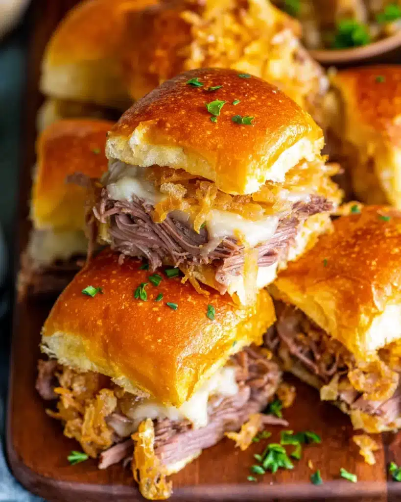 French Dip Sliders 1 Golden French dip sliders with roast beef, melted cheese, and crispy onion topping on a wooden board
