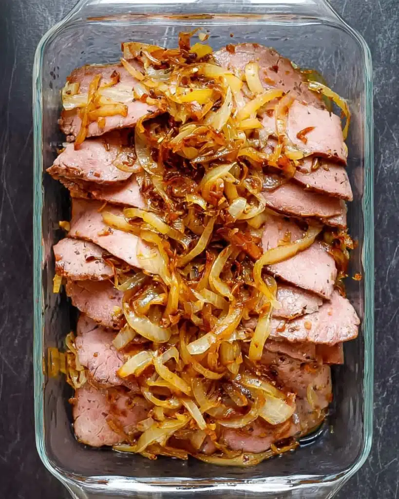 French Dip Sliders 3 Roast beef layered with caramelized onions in a glass baking dish for French Dip Sliders