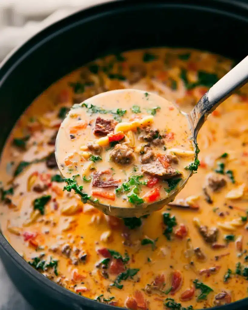 Ladle of creamy sausage pasta soup with kale and carrots