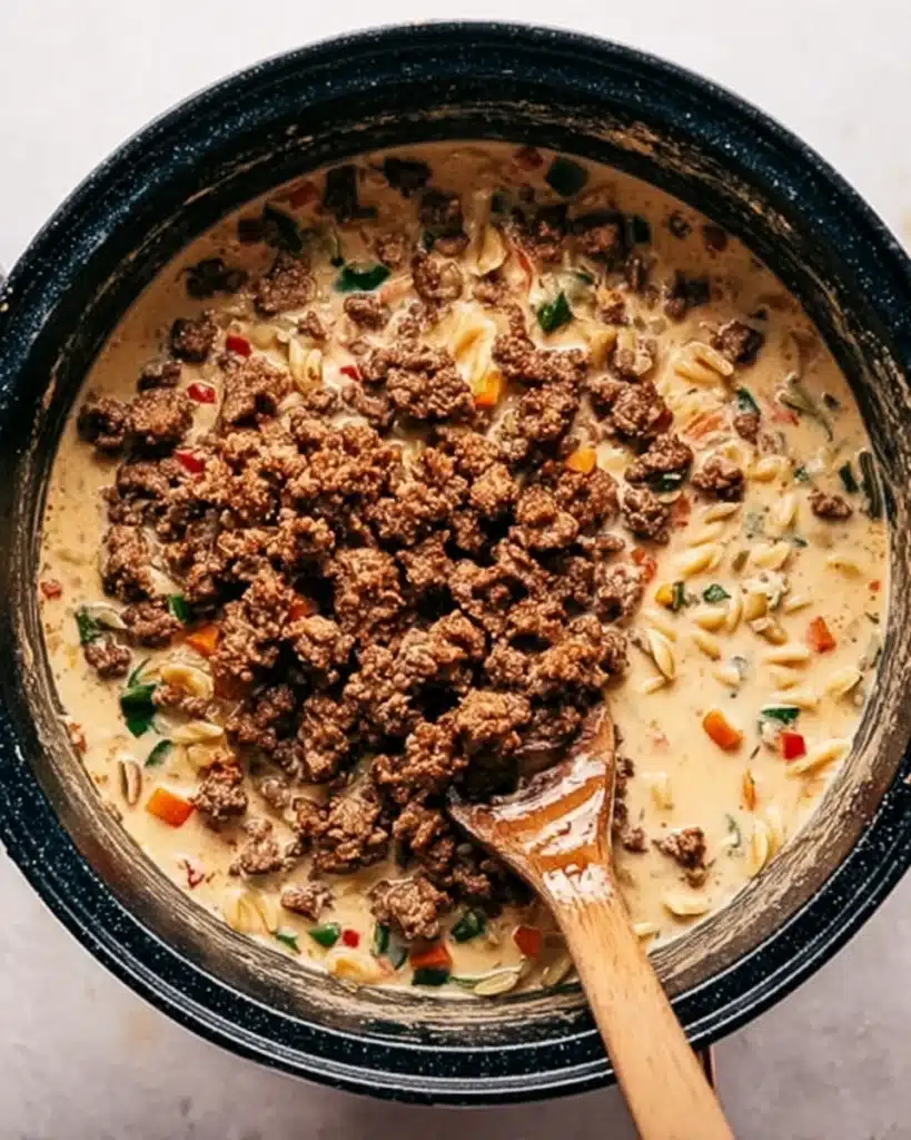 Adding browned sausage to creamy pasta soup in pot