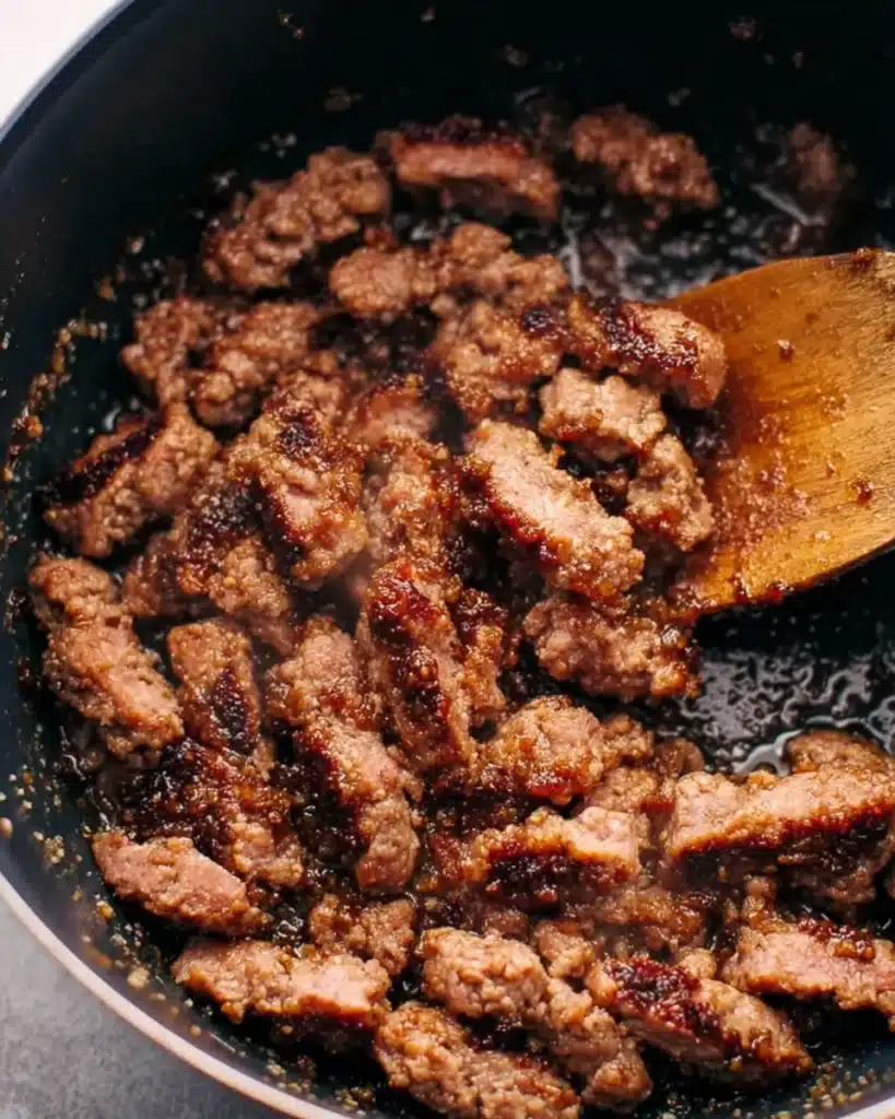Browned Italian sausage in pot with wooden spoon