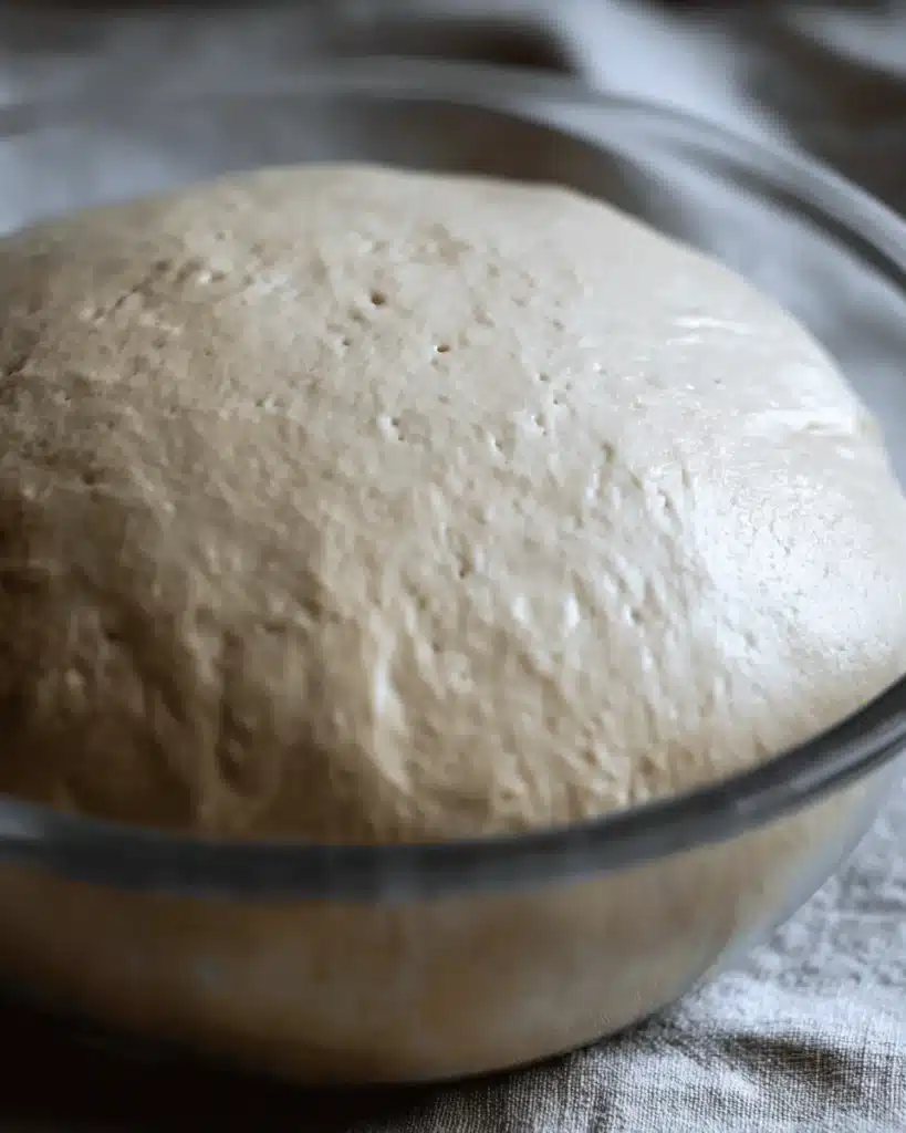 The Best Sourdough Bagels 2 Risen sourdough bagel dough in a glass bowl after overnight fermentation