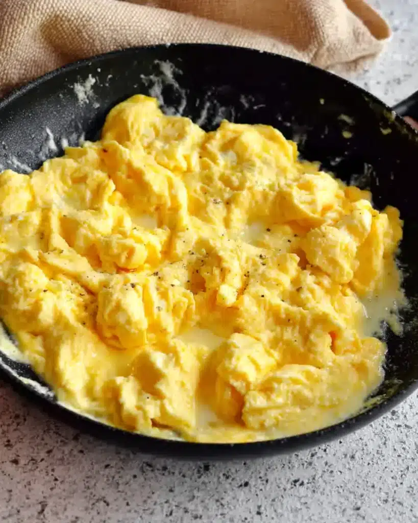 Soft scrambled eggs cooking in a black skillet for breakfast burritos