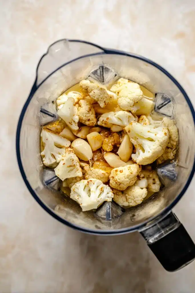Cheddar Cauliflower Soup 3 Blender filled with roasted cauliflower, garlic, and broth for cheddar cauliflower soup