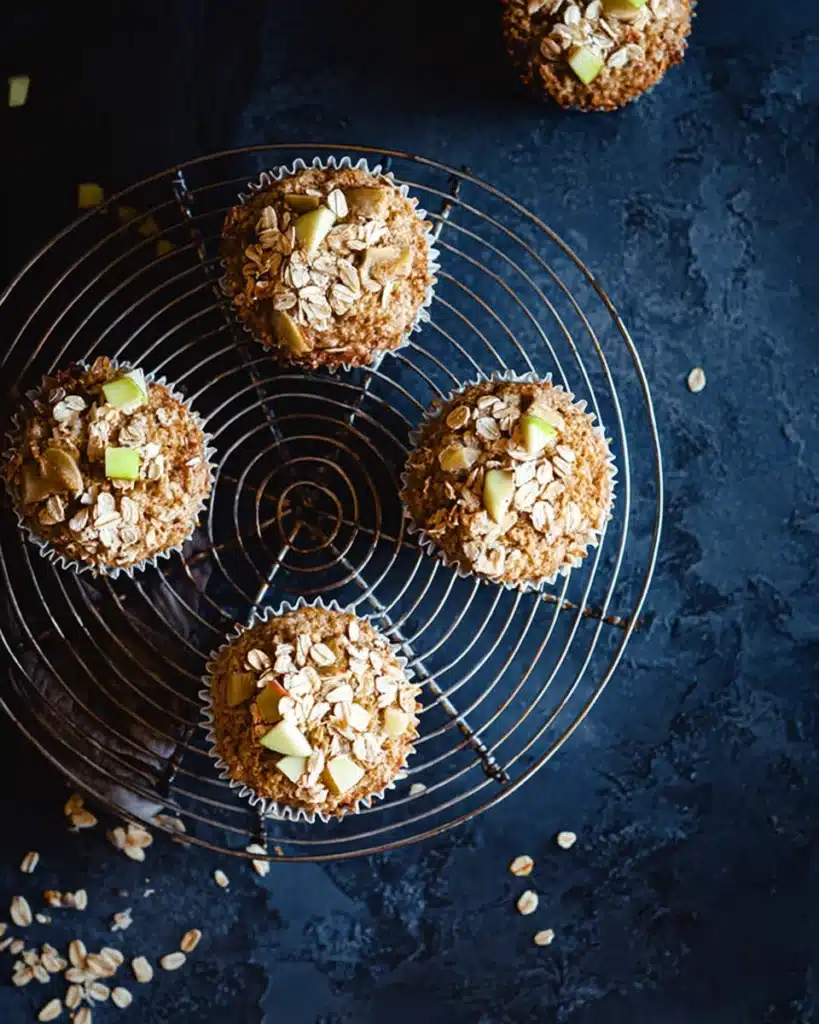 Cinnamon apple oatmeal muffins on a wire cooling rack with oats and apple pieces