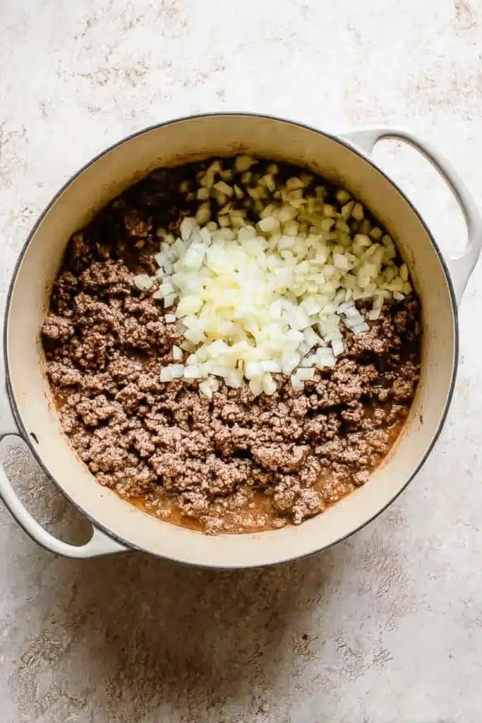 Creamy Taco Soup cooking process with ground beef, diced onion, and garlic in a pot