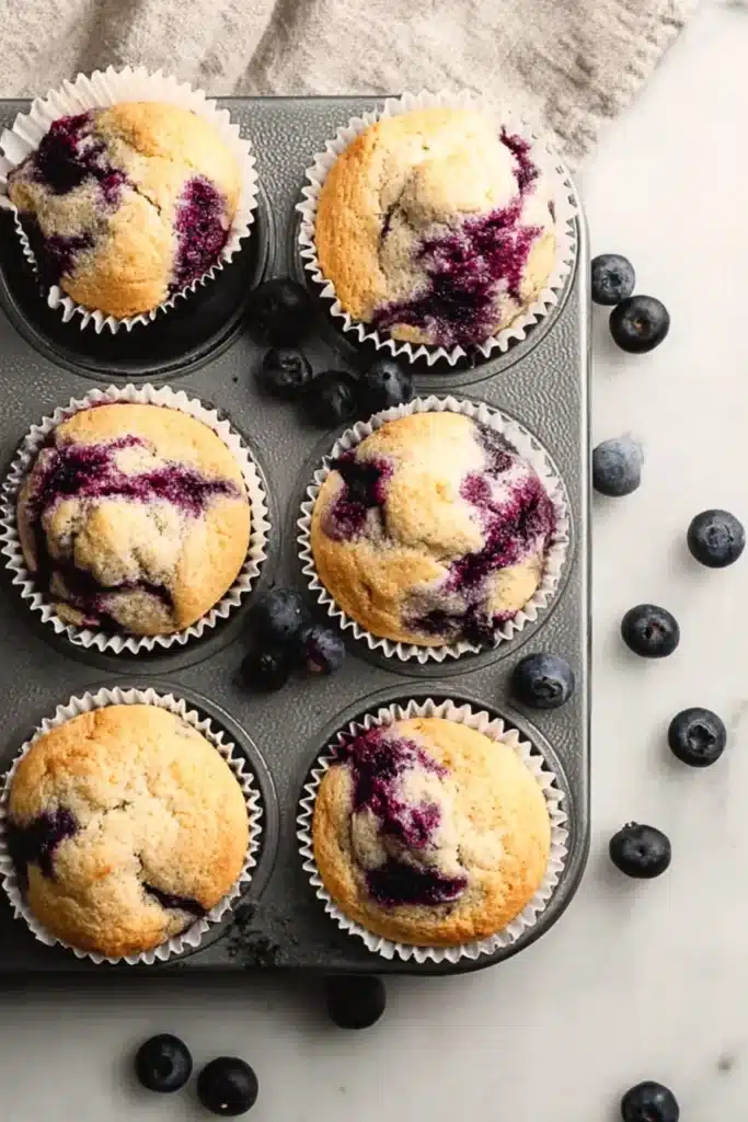 Homemade Blueberry Protein Muffins (Moist, High-Protein, Ready in Under 30 Minutes) 2 Homemade Blueberry Protein Muffins with golden tops and juicy blueberries in a muffin pan