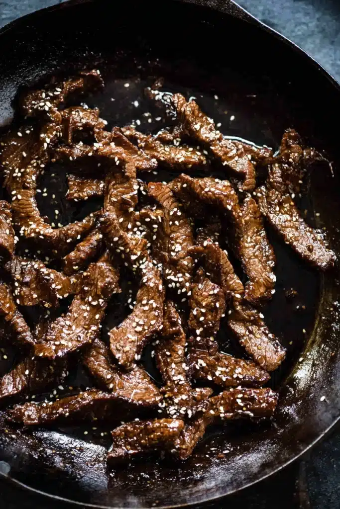 Korean BBQ steak cooking in skillet with sesame seeds