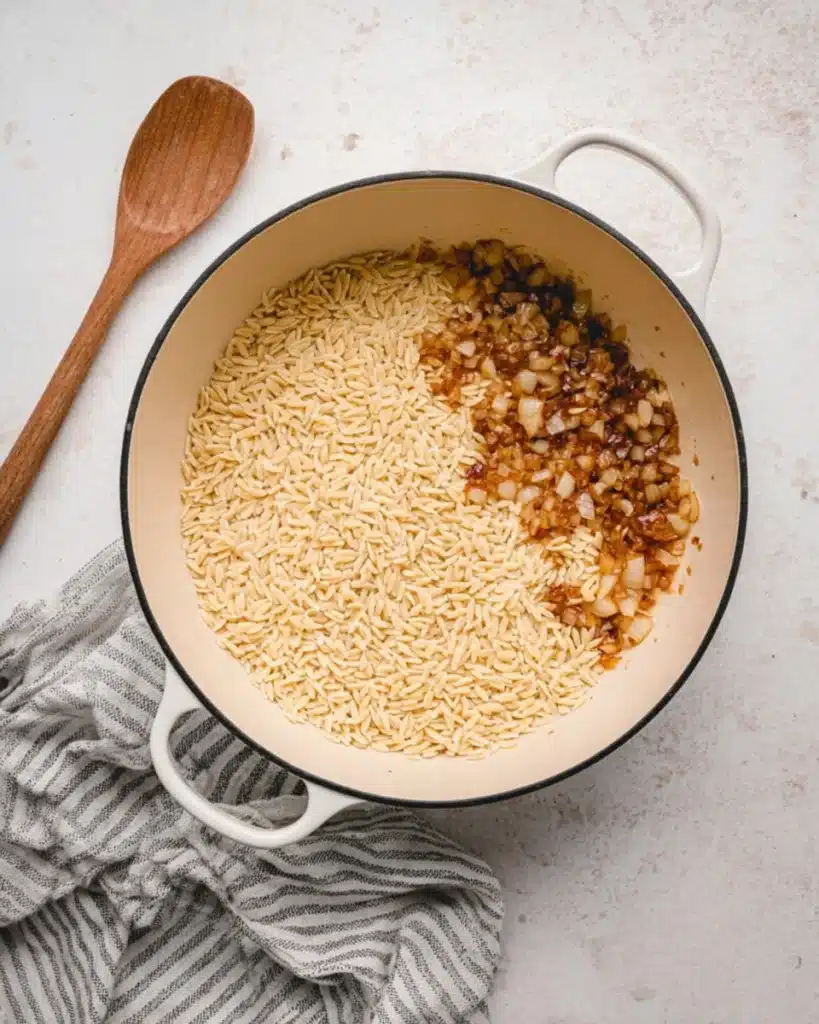 Dry orzo and sautéed onions in a white pot for One Pot Chicken Orzo recipe