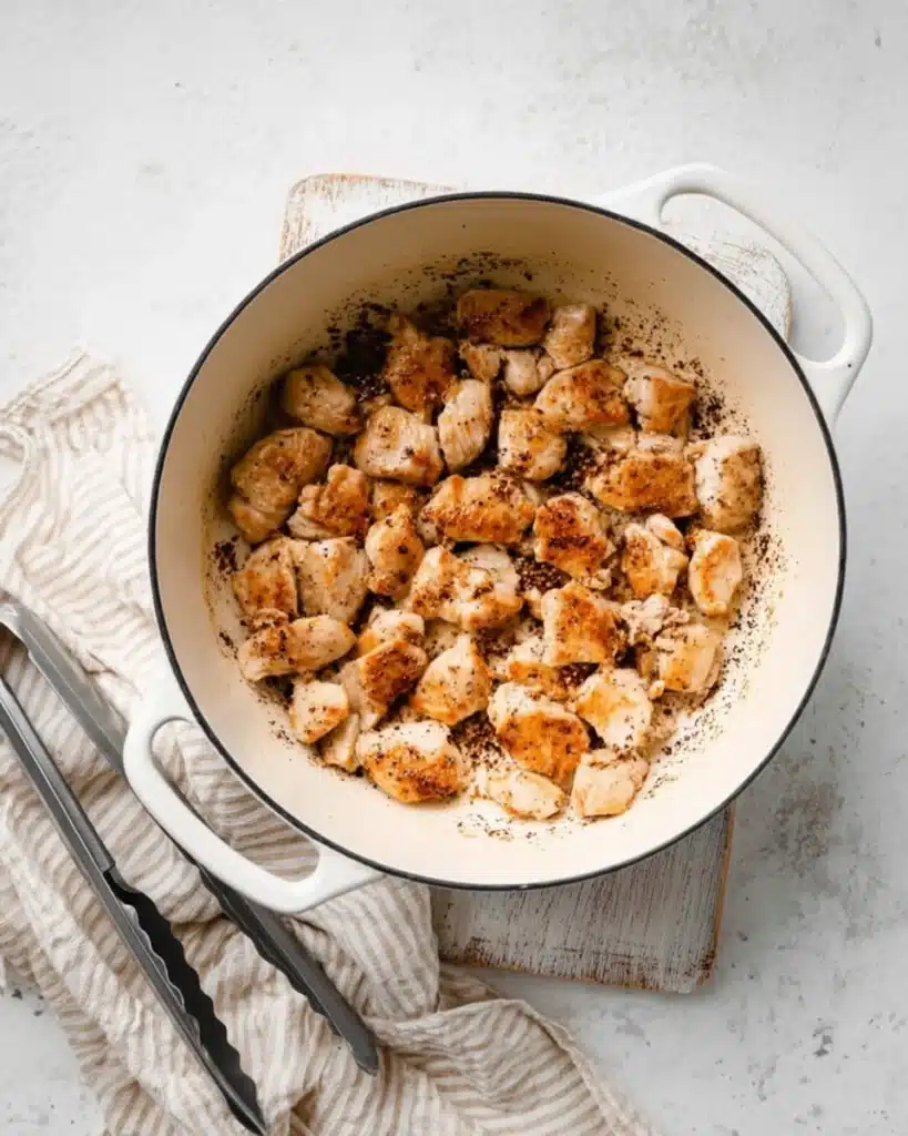 Golden seared chicken pieces in a white pot for One Pot Chicken Orzo recipe